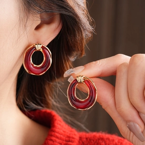 Close-up of elegant gold and red resin round stud earrings worn on a model's ear