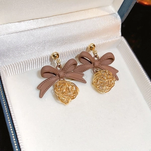 Macro view of brown bow stud earrings with golden woven metal ball pendants in a gift box