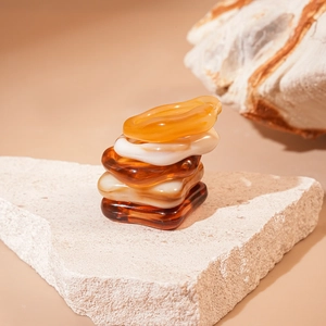 Gros plan de cinq bagues en résine ambre et crème empilées sur une surface en pierre naturelle