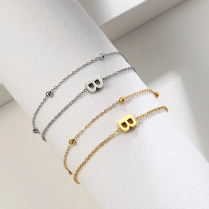 Detail of gold and silver double-layered chain bracelets with letter B pendant