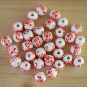 Macro shot of ceramic round beads with red plum blossom patterns on light wood background