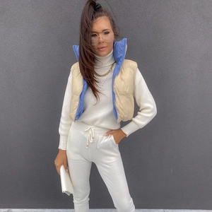 Detail of a women's beige down vest with blue lining over a white knit tracksuit set