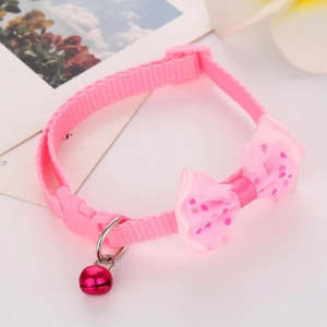 Detailed close-up of pink polka dot bow pet collar with metallic bell on tabletop