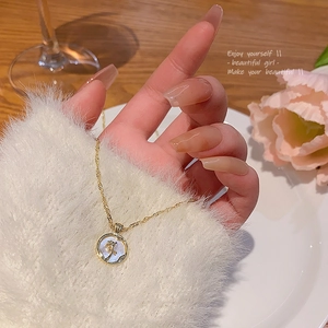Dettaglio della collana a rosa dorata con ciondolo in madreperla su maglione bianco