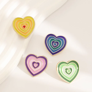 Set of four heart-shaped rainbow enamel pins with gold trim on a white textured background