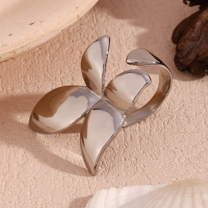Close-up of polished silver clover ring on a neutral textured surface with shells