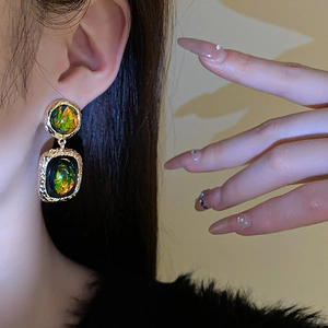 Gros plan d'un mannequin portant des boucles d'oreilles dorées avec résine verte et aiguilles