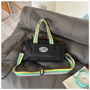 Detail of black nylon sports bag with striped handles and TOCHASO patch on a grey sofa