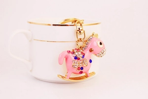 Pink rocking horse keychain with crystals hanging on a white coffee cup edge