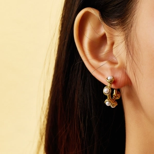 Detailed close-up of a vintage C-shaped gold earring with white pearls on a model