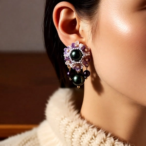 Detail view of purple floral earrings with dark green pearl pendants and gold metal finish