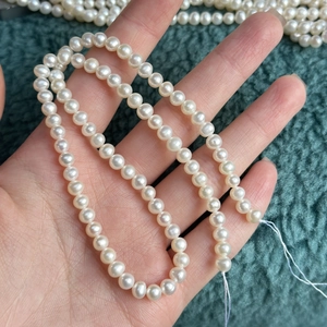 Handheld 4-5mm natural white freshwater pearl necklace on green textured background