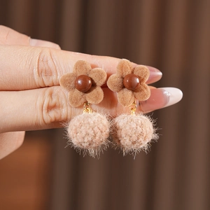 Close-up of brown flocked flower and soft pompom earrings with elegant gold accents