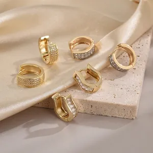 Three elegant gold hoop earrings with zircon stones on silk and stone background