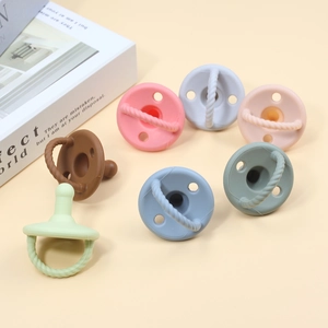 Flat lay of colorful soft silicone baby pacifiers with handle rings on beige background