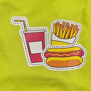 Close-up of fast food cartoon iron-on patches with soda and fries on green fabric