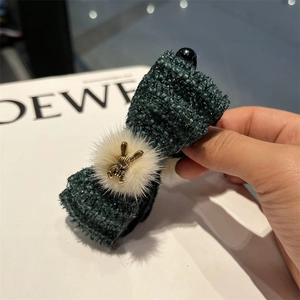 Close-up of elegant dark green tweed bow hair clip with beige pom-pom and gold bunny detail