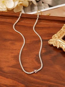 Detail view of a gold floral tennis necklace with purple petals on a wooden tray