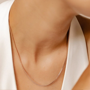 Detail of a rose gold box chain necklace shown on a model neck with a white shirt