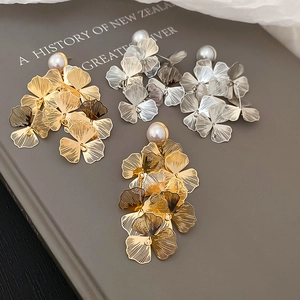 Macro detail of brushed metal flower earrings with pearls on a textured background
