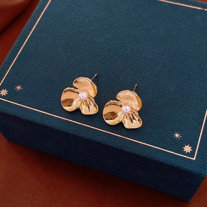 Macro view of golden flower stud earring with pearl center on green jewelry box