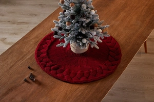 Detail of red cable-knit Christmas tree skirt on a wooden table with a mini tree