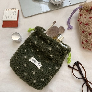 Detail of plush green drawstring pouch with white polka dots on cozy desk background