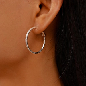 Close-up of silver geometric hoop earrings with a matte texture worn by a model