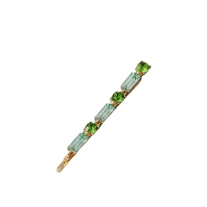 Detail of gold hair clip with round dark green and rectangular light green crystals