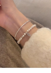 Detailed macro view of S925 silver lucky charm and layered freshwater pearl bracelet