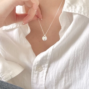 Close-up of minimalist irregular silver pendant necklace worn on a white shirt