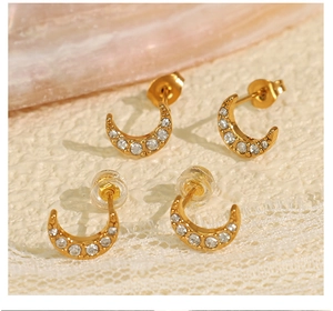 Vue macro de boucles d'oreilles lune dorées serties de zircons sur dentelle et marbre