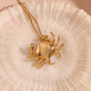 Macro shot of 18K gold-plated crab pendant with thin link chain on white coral base