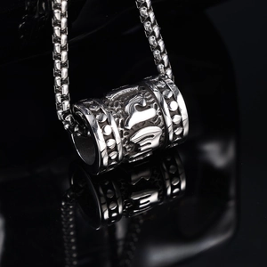 Macro shot of stainless steel mantra cylinder pendant with intricate carved details