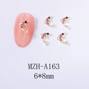 Close-up of dolphin-shaped nail charms in gold alloy with pink and black rhinestones