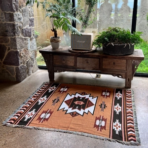 Close-up of bohemian woven blanket with orange geometric patterns and decorative tassels