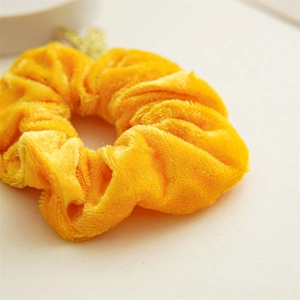 Detailtextur des gelben Samt-Scrunchies mit goldenem Herzanhänger aus Pailletten