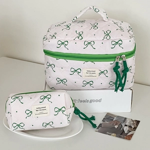 Detail of white quilted cosmetic bag set featuring green bow print and woven zippers