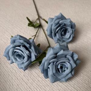 Detailed view of three dusty blue silk roses with green leaves for wedding decor