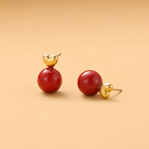 Close-up of heart-shaped gold studs with glossy red glazed spheres and metallic texture