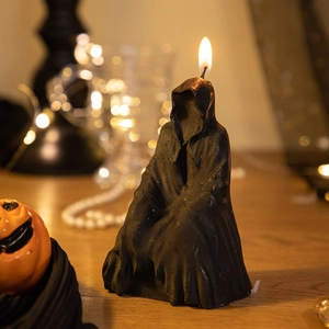 Detailed close-up of a black grim reaper candle with a warm flickering flame and pumpkin decor