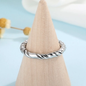 Minimalist silver twist ring with woven design displayed on a wooden stand
