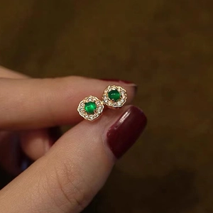Detail of flower-shaped golden earrings with green emerald-cut stones and small zircons