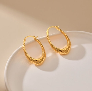 Detail view of 18K gold plated oval hoop earrings with irregular hammered metal texture