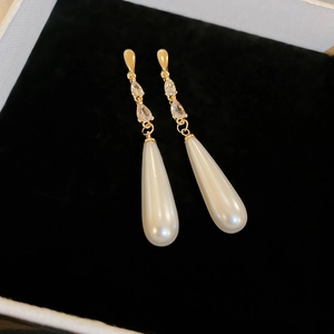 Vue détaillée de longues boucles d'oreilles dorées avec perles gouttes et zircon sur velours