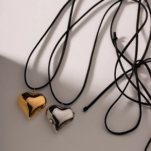 Vue macro de pendentifs cœur or et argent avec cordons noirs sur un fond géométrique