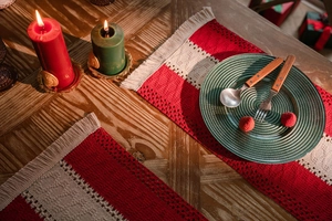 Close-up of red and white woven Christmas placemat with tassels on a wooden table