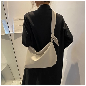 Detail of minimalist cream crossbody bag featuring knot shoulder strap on black coat
