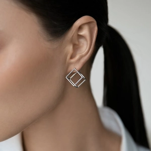 Close-up of minimalist silver hollow cube stud earrings worn by a model on a neutral background