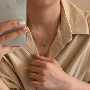 Mirror selfie showing a layered minimalist gold oval necklace on a model wearing a khaki shirt